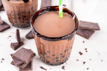 Tasty hot chocolate bubble tea. Cocoa hot or cold beverage with with tapioca balls and dark chocolate syrup, sweet dessert drink on white table with crushed chocolate 