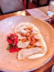 Traditional dumplings served with sour cream, crispy fried onions, and fresh microgreens. Comforting Eastern European dish with rustic presentation and warm, homemade flavors.