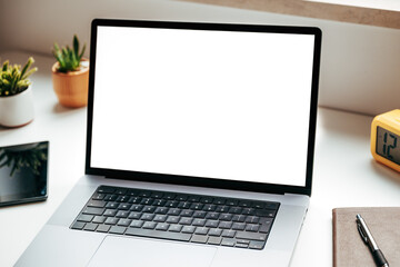 Open laptop with blank mockup screen on white office desk beside notebook, digital tablet and potted cactus plants, modern workspace concept.