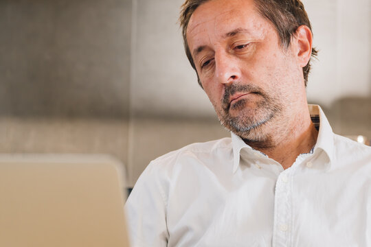 Tired overworked businessman with facial hair stubble tilting his head while looking at laptop screen in home office, fatigue and overwork concept. - Powered by Adobe