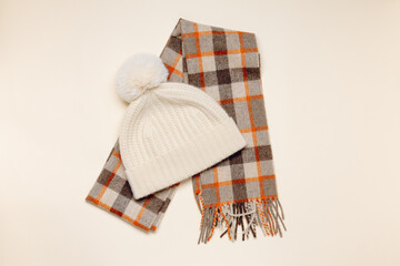 Warm knitted hat with checkered scarf top view on beige background