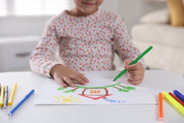 Little girl drawing with felt pen at white table indoors, closeup