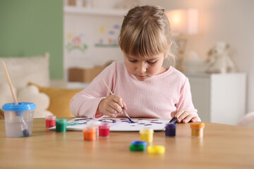 Little girl with brush drawing at wooden table indoors