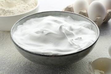 Beating egg whites in bowl, eggshell and flour on grey textured table, closeup