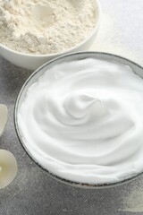Beating egg whites in bowl and flour on grey textured table, closeup