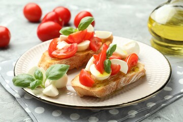 Tasty bruschettas with mozzarella cheese, tomatoes and basil on grey textured table, closeup