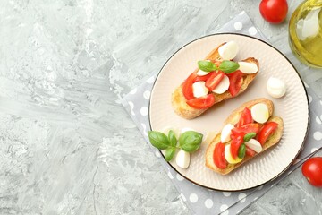 Tasty bruschettas with mozzarella cheese, tomatoes and basil on grey textured table, flat lay. Space for text