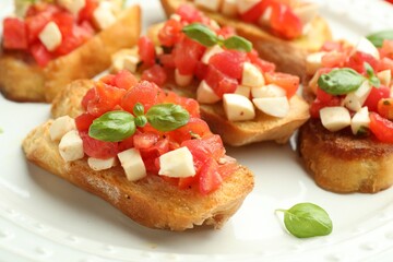 Tasty bruschettas with mozzarella cheese, tomatoes and basil on white plate, closeup