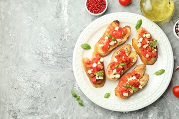 Tasty bruschettas with mozzarella cheese, tomatoes, basil and spices on grey textured table, flat lay. Space for text