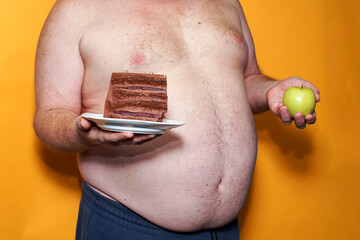 A green apple and a piece of cake on the background of a man's fat belly. Concept in the choice of food and nutrition.