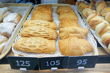 Freshly baked buns and pies made from wheat bread are on display for sale on a shelf in the store.
