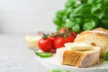 Slices of baguette with butter, basil and tomatoes on light grey table, closeup. Space for text
