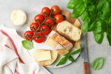 Slices of baguette with butter, basil, tomatoes and knife on light grey table, flat lay