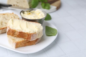 Slices of baguette with butter, basil and knife on white tiled table, closeup. Space for text