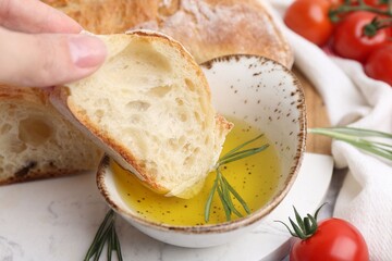 Woman dipping piece of baguette into oil at table, closeup