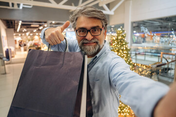 Selfie time, with packages. Senior man is in the mall, shopping time conception