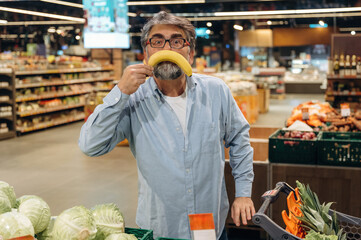 Making fun face with banana. A senior man is buying food in the grocery store