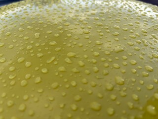 The glossy yellow surface is covered with numerous water drops, creating a dynamic and material visual effect.