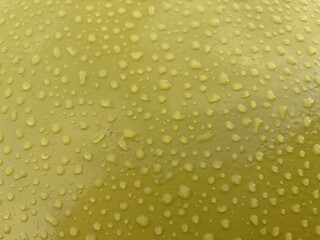 The glossy yellow surface is covered with numerous water drops, creating a dynamic and material visual effect.