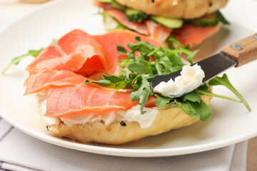 Delicious bagels with salmon, cream cheese, cucumber and arugula on table, closeup