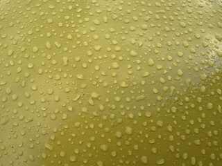 The glossy yellow surface is covered with numerous water drops, creating a dynamic and material visual effect.
