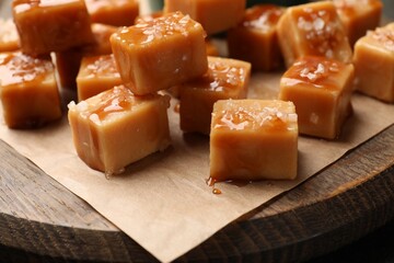 Tasty candies with salt and caramel sauce on wooden board, closeup