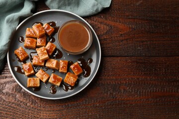 Tasty candies with salt and caramel sauce on wooden table, top view. Space for text