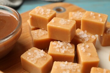 Tasty candies with salt and caramel sauce on light blue table, closeup