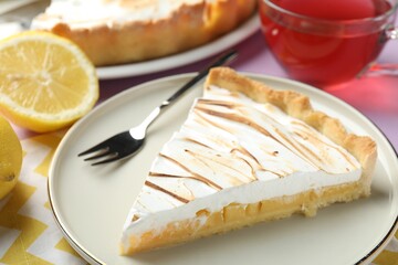Slice of tasty lemon meringue tart served on lilac table, closeup