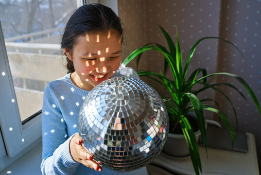 Teenage girl enjoying sunlight with disco ball indoors