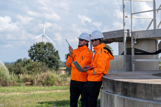 Engineers collaborate on wind farm project while discussing plans and data from the control center near the turbines - Powered by Adobe