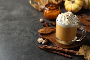 Tasty pumpkin latte with whipped cream in glass cup, spices and autumn decor on grey table, closeup. Space for text