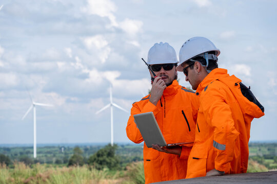 Two workers collaborate on a laptop while inspecting a wind farm during daylight hours in a rural area - Powered by Adobe