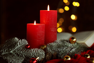 Burning candles, fir tree branches, baubles and sweater against black background with blurred lights, closeup. Bokeh effect