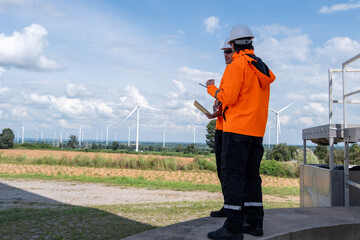 Workers conduct maintenance checks at a wind farm with turbines in the background during a clear sunny day