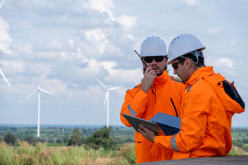 Workers in bright jackets oversee wind farm operations while discussing tasks with a laptop and radio