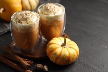 Tasty pumpkin latte with whipped cream, spices and fresh vegetable on black table, closeup. Space for text