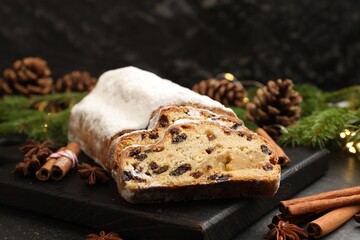 Traditional Christmas Stollen with icing sugar, spices and festive decor on black table, closeup