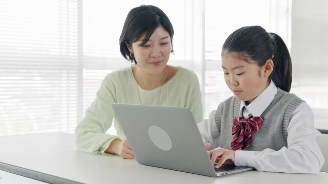 教室で女性教員からパソコンを教わる女の子