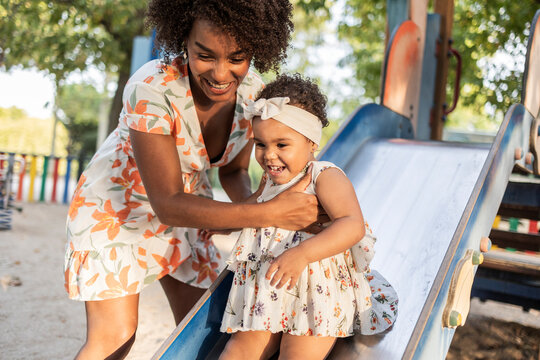Smiling mother guiding child down slide at playground