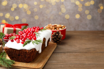 Tasty Christmas cake with icing, cranberries, rosemary and festive decor on wooden table against background with blurred lights, closeup. Space for text