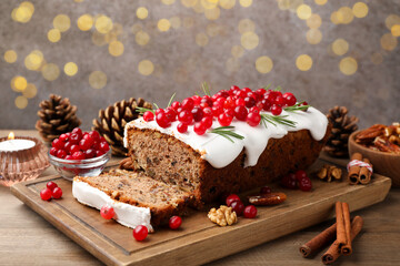 Tasty Christmas cake with icing, cranberries and rosemary on wooden table against background with blurred lights, closeup