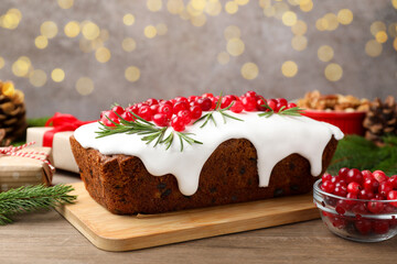 Tasty Christmas cake with icing, cranberries, rosemary and festive decor on wooden table, closeup