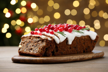 Tasty Christmas cake with icing, cranberries and rosemary on wooden table against background with blurred lights, closeup