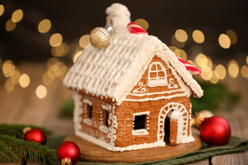 Beautiful gingerbread house and ornaments on wooden table against blurred lights, closeup. Christmas treat