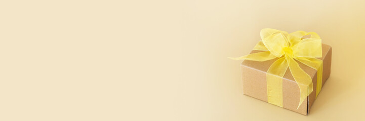 Gift box with yellow bow on pastel beige background. Gift for holiday, birthday, Wedding, Mother's Day, Valentine's day. Floral arrangement. Banner