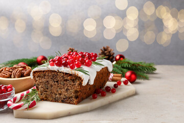 Tasty Christmas cake with icing, cranberries, nuts and festive decor on light grey table against blurred lights, space for text. Bokeh effect
