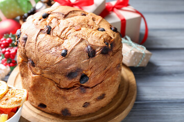 Tasty Christmas panettone cake and gift boxes on grey wooden table.