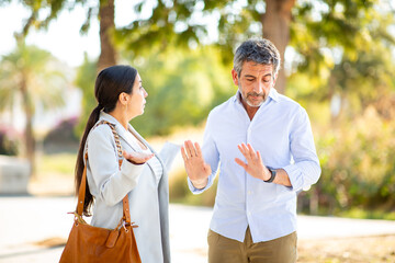Couple arguing with defensive gestures in a heated outdoor discussion
