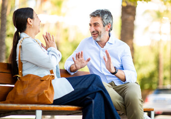 Joyful couple enjoying lively conversation with gestures on a bench
